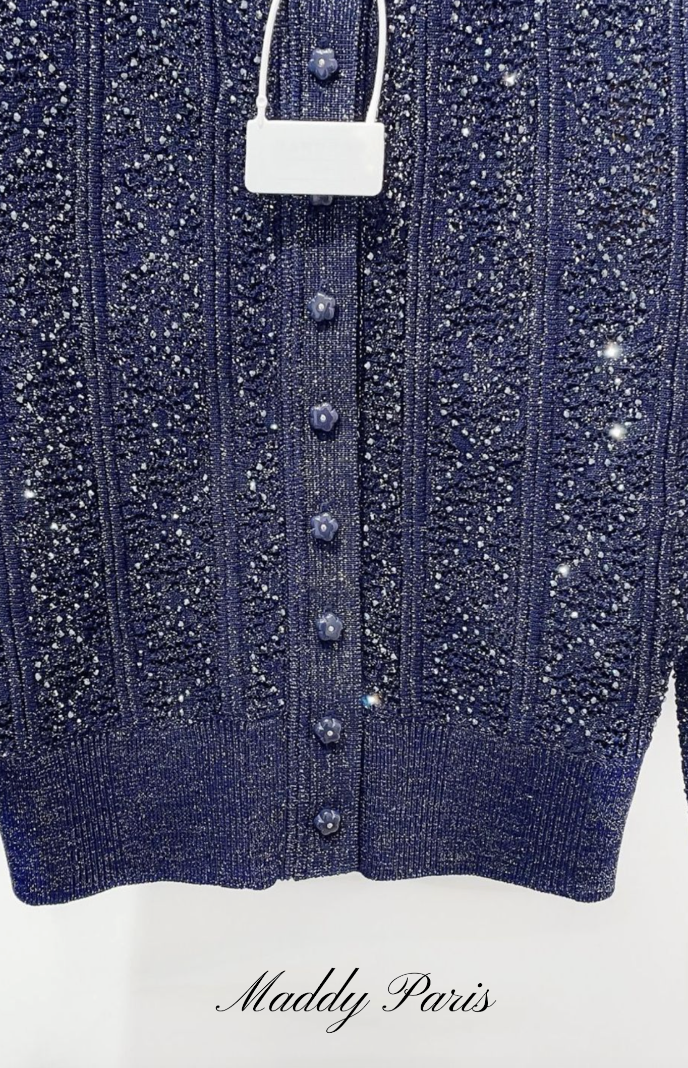 Close-up of a blue cardigan with buttons and sparkling details, featuring the brand 'Maddy Paris'.